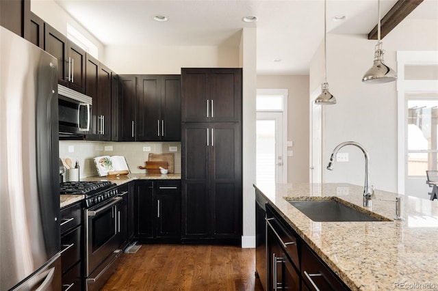 kitchen with light stone countertops, tasteful backsplash, a sink, dark wood finished floors, and stainless steel appliances