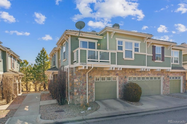 view of property featuring a garage, concrete driveway, a balcony, stone siding, and a chimney