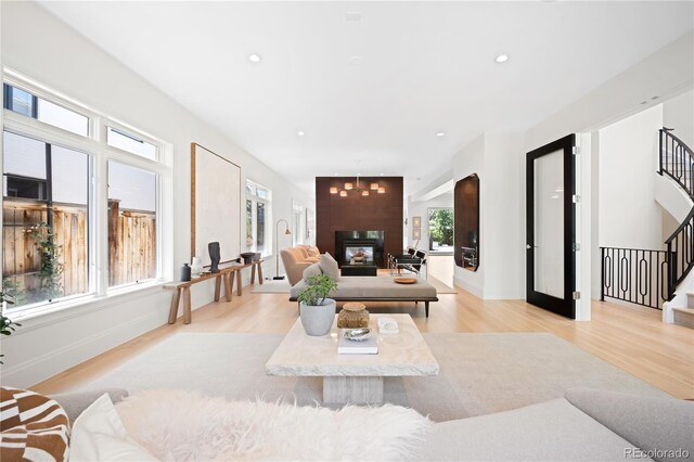 living area featuring stairway, light wood-style floors, recessed lighting, baseboards, and a glass covered fireplace