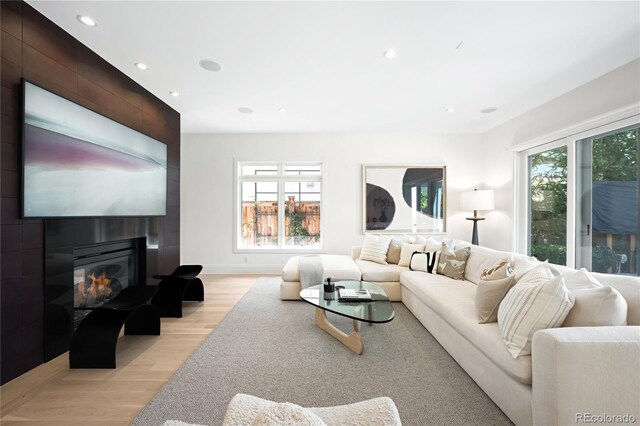 living room featuring light wood finished floors, recessed lighting, a large fireplace, and baseboards