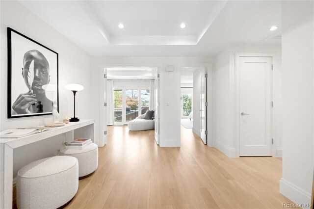hall featuring light wood-style floors, a raised ceiling, baseboards, and recessed lighting