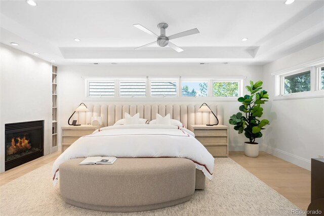 bedroom featuring a raised ceiling, wood finished floors, recessed lighting, and a lit fireplace