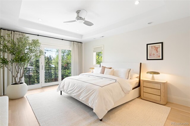 bedroom with access to outside, a tray ceiling, light wood-style floors, recessed lighting, and ceiling fan