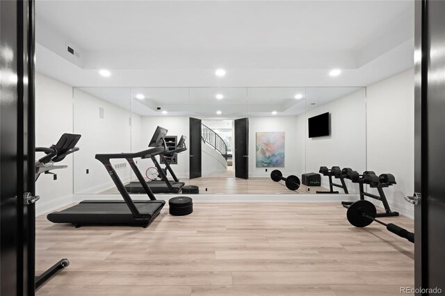 exercise area with wood finished floors, baseboards, recessed lighting, and a raised ceiling