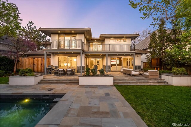 back of house at dusk featuring a balcony, an outdoor hangout area, stucco siding, an outdoor pool, and a patio area
