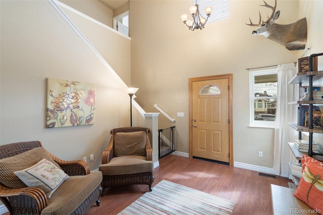 foyer with visible vents, baseboards, a high ceiling, wood finished floors, and a notable chandelier