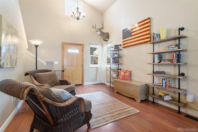 living area featuring wood finished floors, visible vents, baseboards, a high ceiling, and a notable chandelier