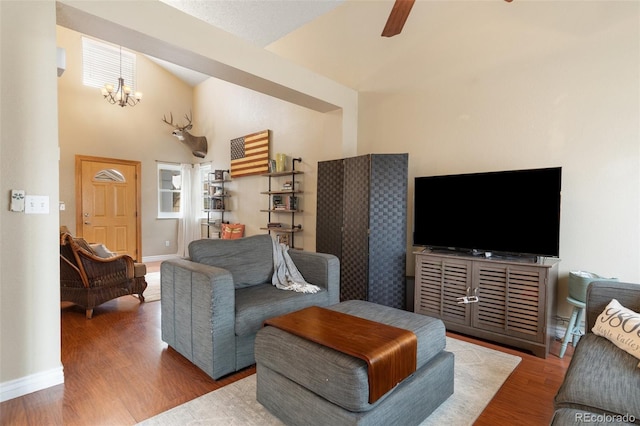 living area with a wealth of natural light, baseboards, wood finished floors, and ceiling fan with notable chandelier