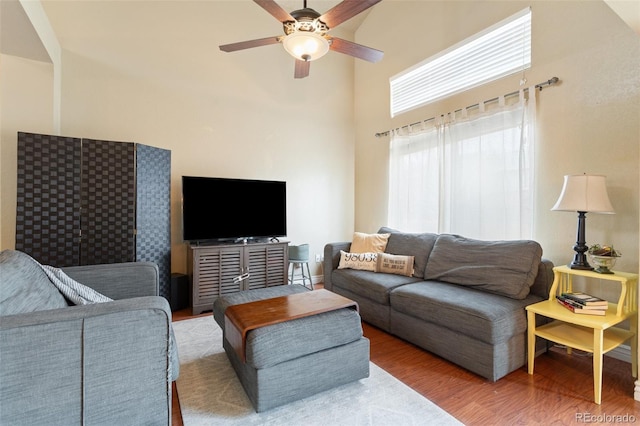 living room with ceiling fan, wood finished floors, and a towering ceiling