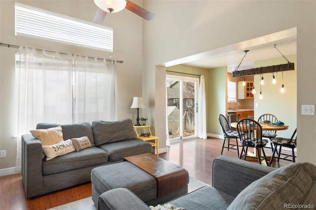 living room with baseboards, a high ceiling, wood finished floors, and a ceiling fan