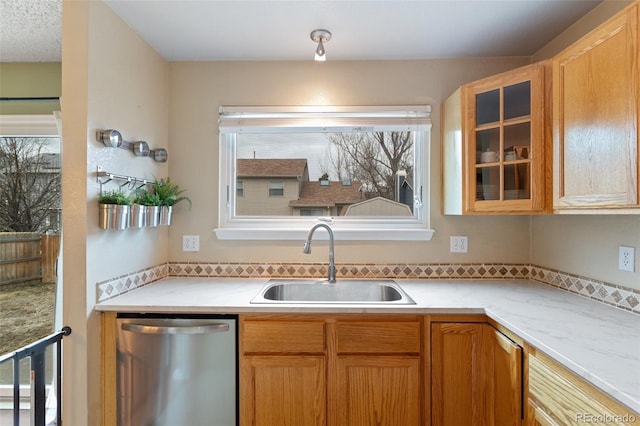 kitchen featuring a sink, glass insert cabinets, stainless steel dishwasher, and light countertops