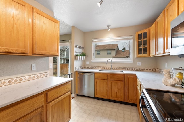 kitchen featuring light floors, a sink, glass insert cabinets, appliances with stainless steel finishes, and a textured ceiling