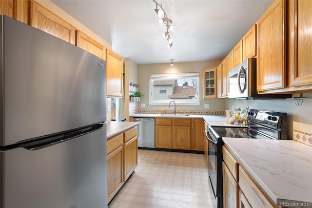 kitchen featuring a sink, glass insert cabinets, light floors, and appliances with stainless steel finishes