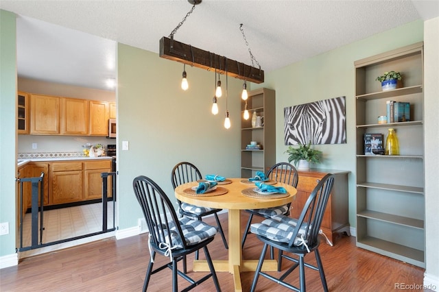 dining room with baseboards, a textured ceiling, and light wood-style flooring