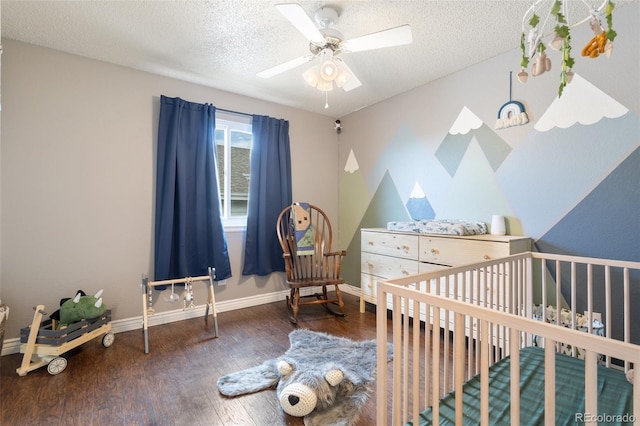 bedroom featuring a ceiling fan, a textured ceiling, wood finished floors, a nursery area, and baseboards