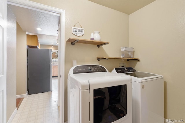 laundry room with baseboards, washing machine and dryer, light floors, laundry area, and a textured ceiling