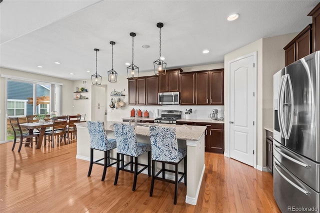 9957 Quintero St, Commerce City, CO 80022 - kitchen with appliances with stainless steel finishes, dark brown cabinetry, a breakfast bar area, light wood-style flooring, and decorative light fixtures