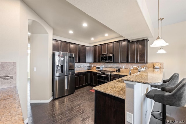 kitchen featuring sink, a breakfast bar, appliances with stainless steel finishes, hanging light fixtures, and kitchen peninsula