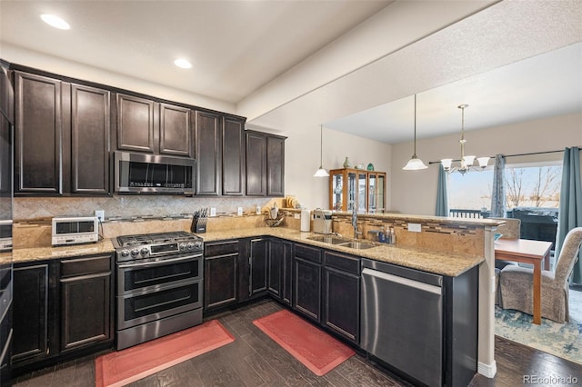 kitchen with appliances with stainless steel finishes, dark hardwood / wood-style floors, kitchen peninsula, and hanging light fixtures