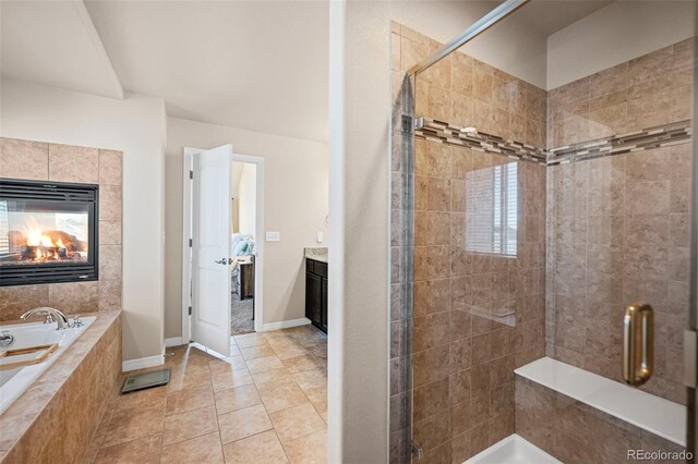 bathroom featuring vanity, plus walk in shower, a tiled fireplace, and tile patterned flooring