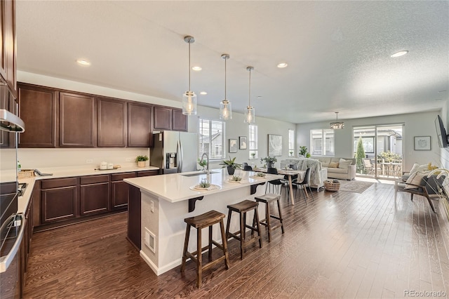 kitchen with dark wood-type flooring, a kitchen bar, stainless steel fridge, and a center island