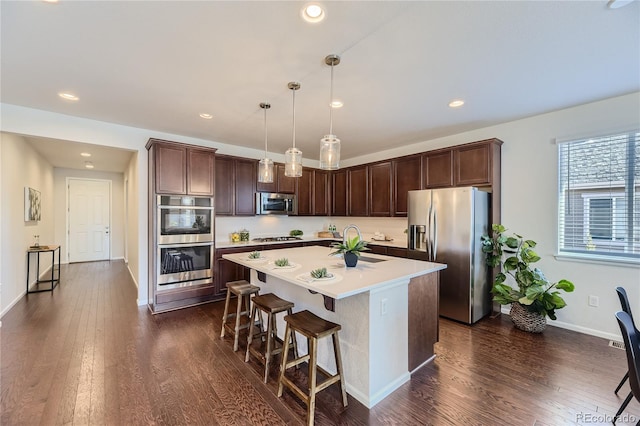 kitchen featuring a center island with sink, stainless steel appliances, a kitchen bar, hanging light fixtures, and dark wood-type flooring