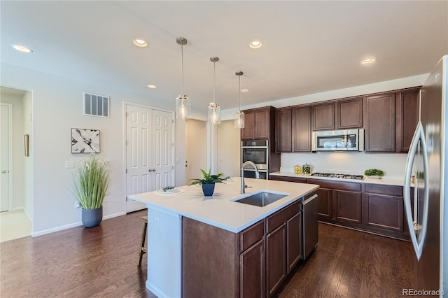 kitchen featuring a kitchen bar, stainless steel appliances, a kitchen island with sink, dark hardwood / wood-style floors, and decorative light fixtures