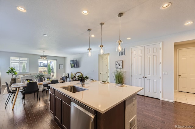 kitchen featuring sink, a kitchen island with sink, stainless steel dishwasher, dark hardwood / wood-style floors, and pendant lighting