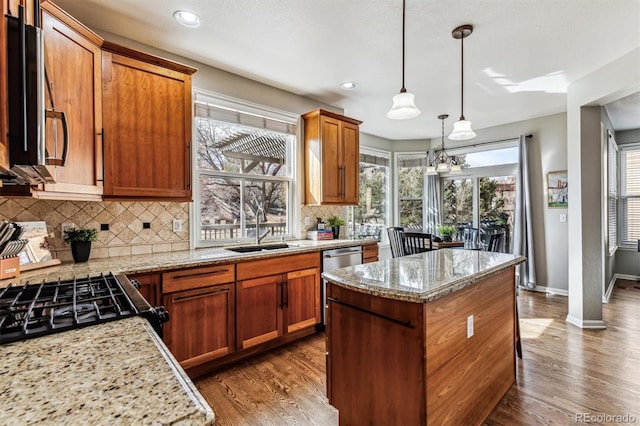 kitchen with sink, decorative light fixtures, a center island, appliances with stainless steel finishes, and light stone countertops