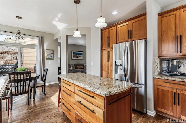 kitchen with light stone counters, decorative light fixtures, stainless steel fridge, and tasteful backsplash