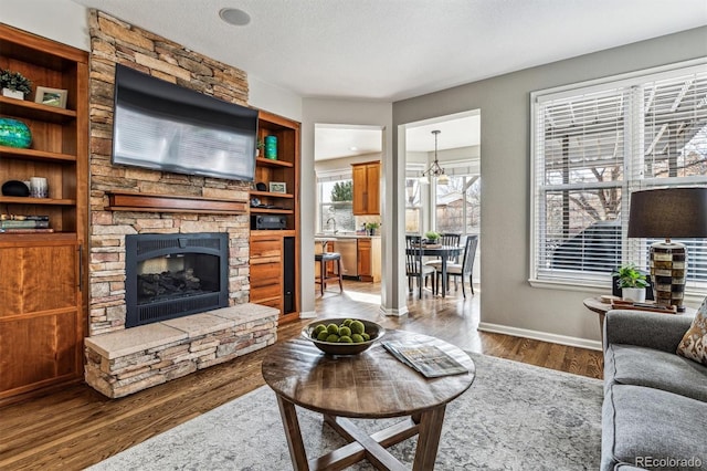 living room with a stone fireplace, wood-type flooring, a chandelier, a textured ceiling, and built in shelves