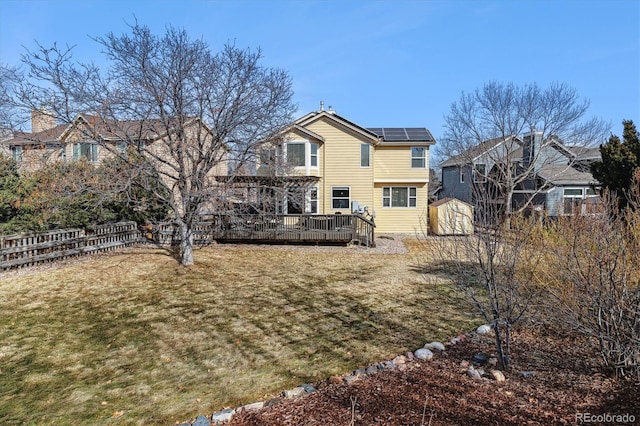 back of property with a yard, a storage unit, solar panels, and a deck