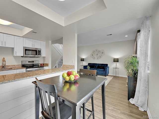 kitchen featuring sink, a tray ceiling, white cabinetry, light hardwood / wood-style floors, and stainless steel appliances