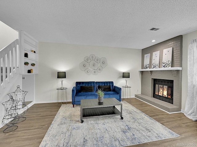 living room with hardwood / wood-style floors, a brick fireplace, and a textured ceiling