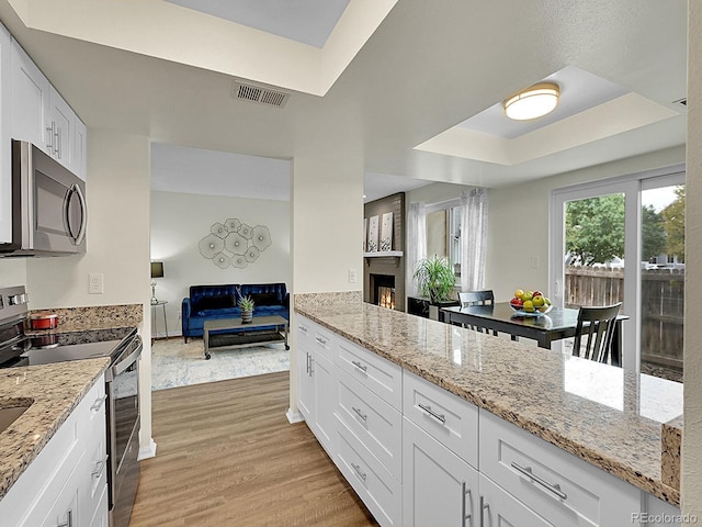 kitchen featuring light stone countertops, appliances with stainless steel finishes, light hardwood / wood-style flooring, and white cabinets