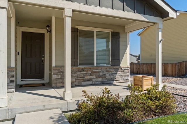 entrance to property featuring stone siding, covered porch, fence, and board and batten siding