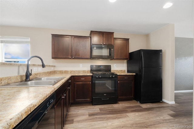 kitchen featuring black appliances, a sink, dark brown cabinets, light countertops, and recessed lighting