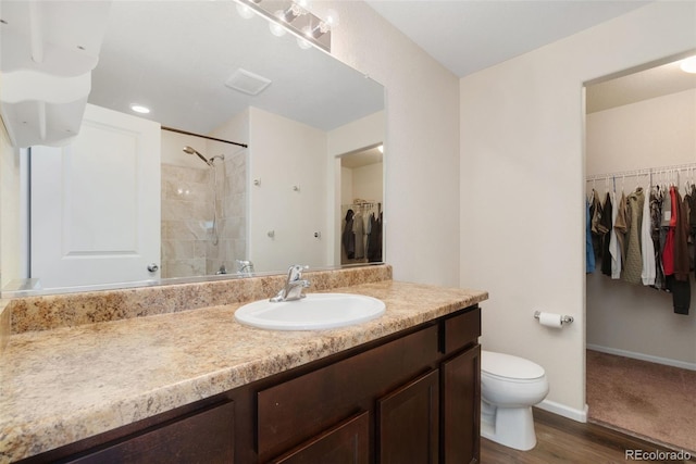 bathroom with toilet, a walk in closet, vanity, wood finished floors, and a shower