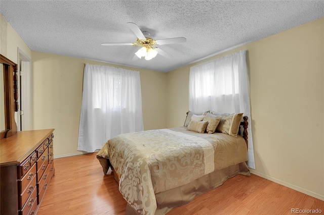 bedroom with ceiling fan, light hardwood / wood-style flooring, and a textured ceiling