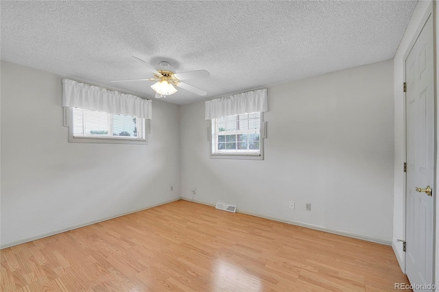 empty room featuring ceiling fan, plenty of natural light, a textured ceiling, and light wood-type flooring