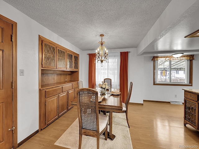 6769 W 70th Ave, Arvada, CO 80003 - dining room with a chandelier, light wood-style flooring, a textured ceiling, and baseboards