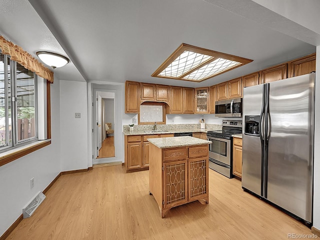 6769 W 70th Ave, Arvada, CO 80003 - kitchen featuring stainless steel appliances, a sink, light wood-style flooring, a kitchen island, and light stone countertops