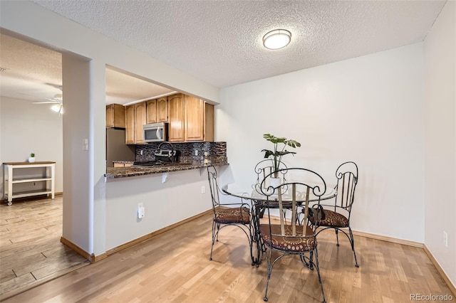 kitchen featuring backsplash, dark stone countertops, a textured ceiling, light hardwood / wood-style floors, and stainless steel appliances