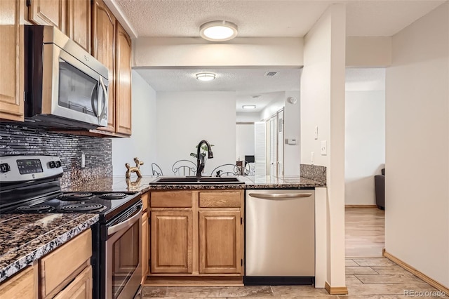 kitchen with backsplash, a textured ceiling, stainless steel appliances, sink, and light hardwood / wood-style floors