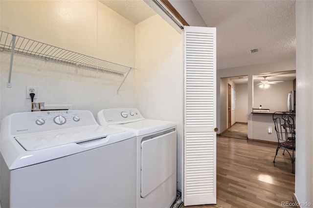 clothes washing area with a textured ceiling, washing machine and dryer, light hardwood / wood-style flooring, and ceiling fan