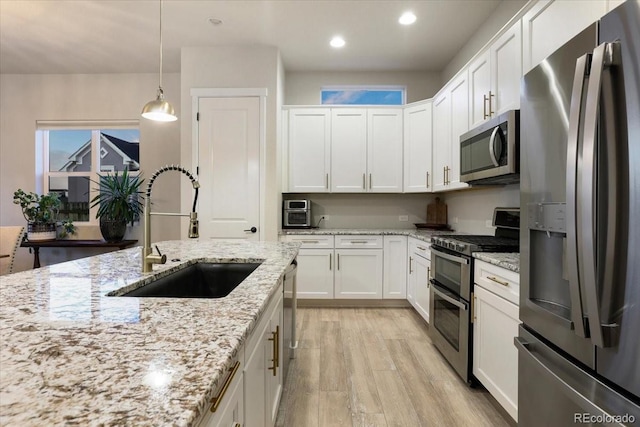 kitchen featuring sink, light stone counters, hanging light fixtures, stainless steel appliances, and white cabinets