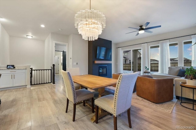 dining room featuring a large fireplace, ceiling fan with notable chandelier, and light hardwood / wood-style floors