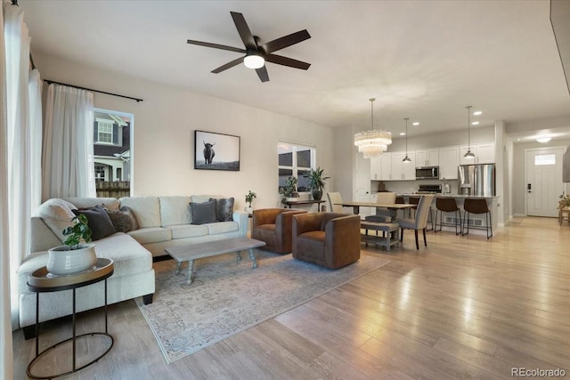 living room featuring ceiling fan with notable chandelier and light hardwood / wood-style floors