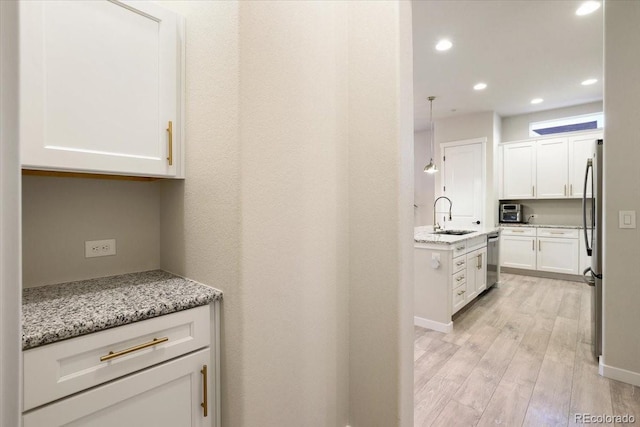 kitchen with sink, appliances with stainless steel finishes, white cabinetry, light stone countertops, and light hardwood / wood-style floors