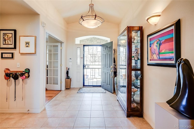 entryway with vaulted ceiling, baseboards, and light tile patterned floors